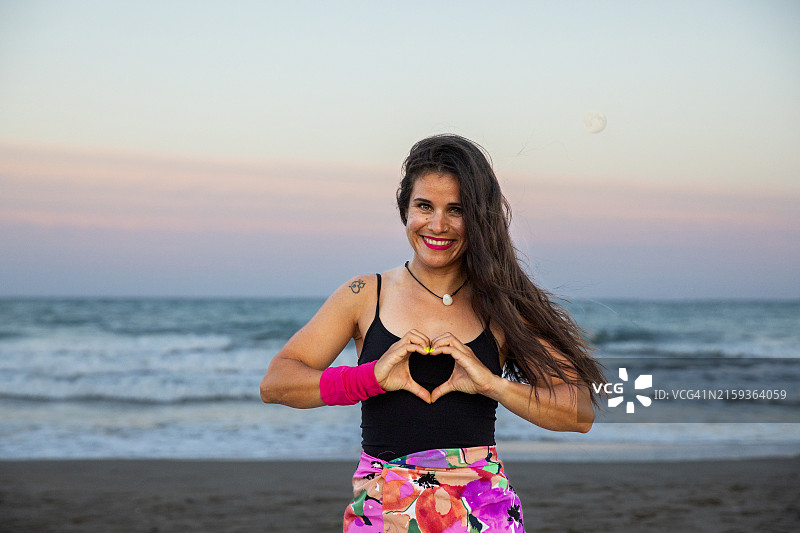 日落时分，海滩上用双手比心的女人图片素材
