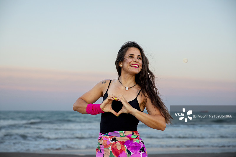 日落时分，海滩上用双手比心的女人图片素材