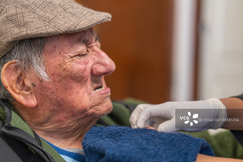护理人员将假牙戴在闭着眼睛的老年男子身上图片素材