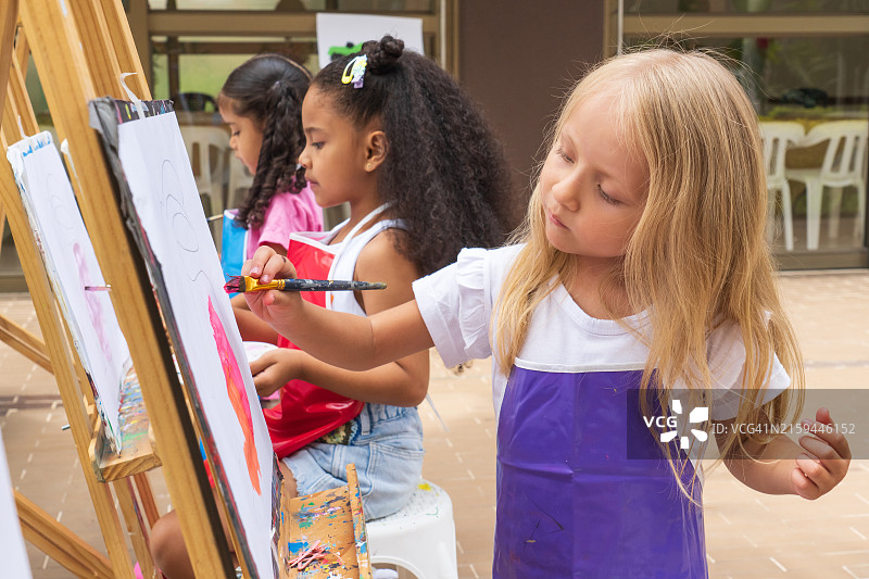 阳光明媚的户外，三个女孩在美术课上一起绘画图片素材