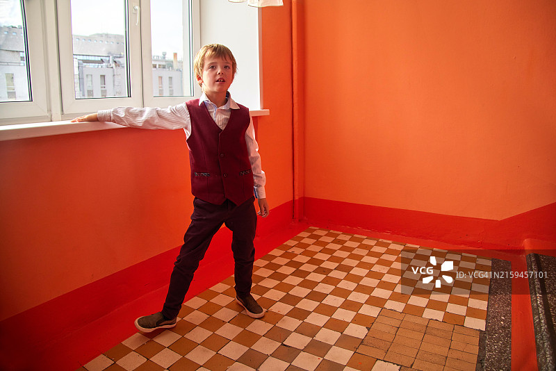 穿着时尚正装，自信地站在充满活力的橙色房间的窗户旁的男孩，散发着经典可爱的氛围图片素材