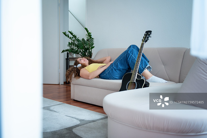在沙发上弹吉他的快乐卷发美女图片素材
