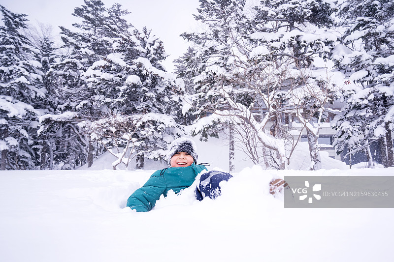 穿着暖和冬装躺在蓬松白雪中快乐的男孩：冬季乐趣图片素材