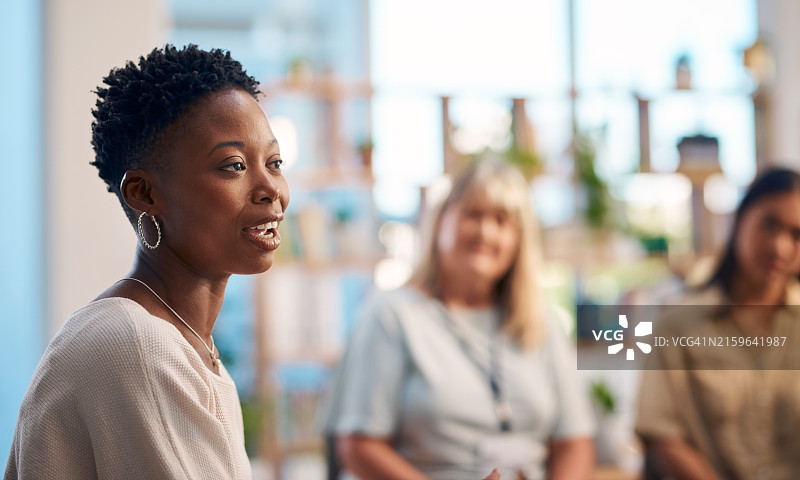 一群人参加支持小组会议，重点关注一个人分享她的想法。环境开放且支持性，鼓励联系和情感支持图片素材