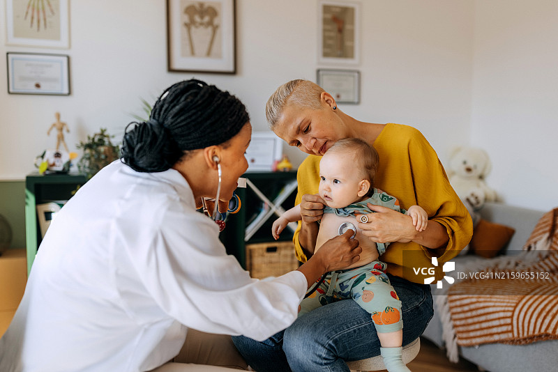 儿科女医生用听诊器检查可爱的男婴，男婴的母亲抱着他图片素材