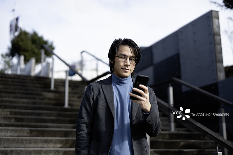 穿着休闲商务装在台阶上对着手机微笑的年轻男人图片素材