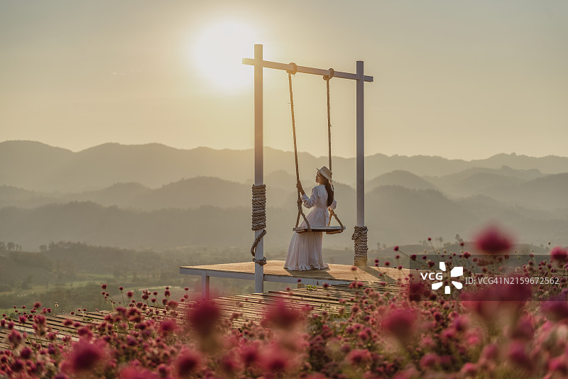 坐在日落时花果园观景台秋千上的女人，在泰国达府Baanrai Aoon Rak花卉农场享受新鲜空气的快乐女人图片素材
