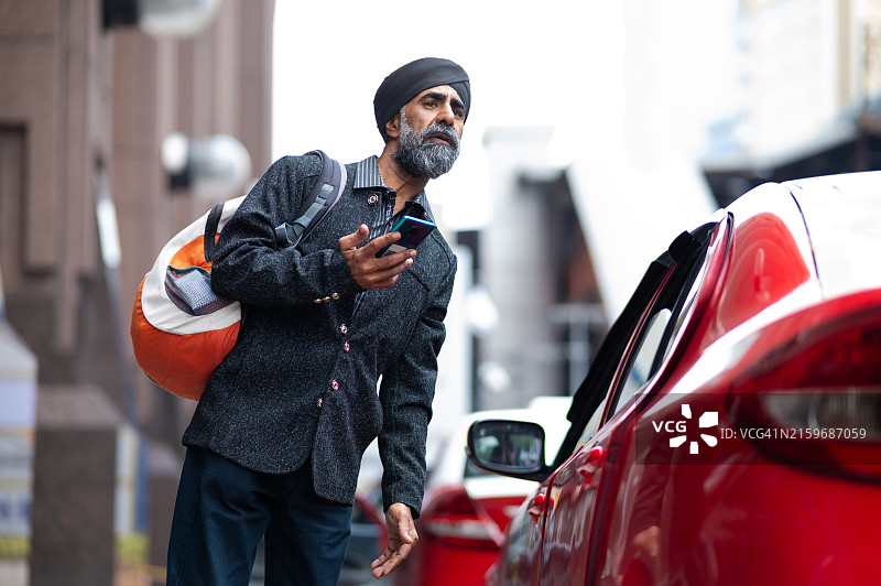 一位戴着头巾的中年锡克族商人正在繁忙的街道上用智能手机叫车图片素材