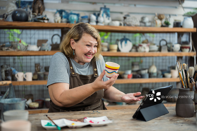 年长的女人在工作室里手绘陶瓷杯图片素材