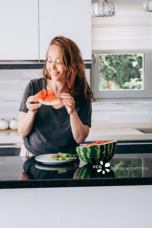 微笑的女性在明亮现代的厨房中享受清凉的西瓜。夏季健康小吃。图片素材