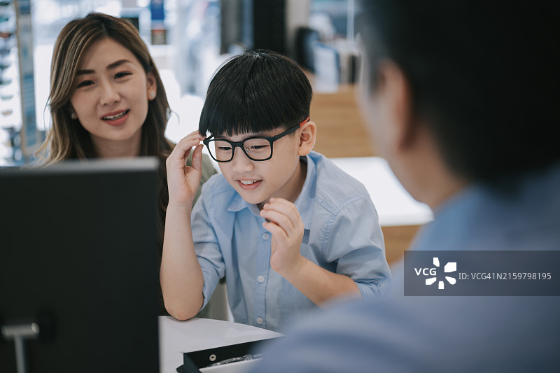快乐中国男孩在眼镜店试戴新眼镜图片素材