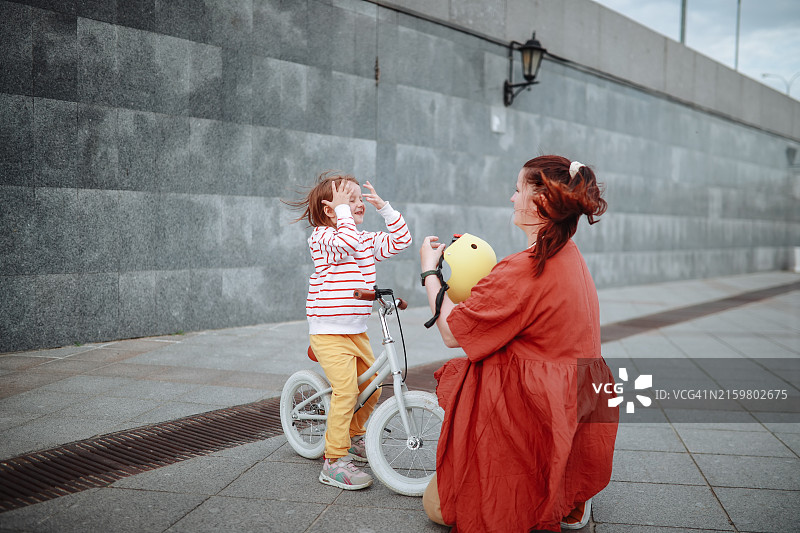 在城市步行期间，帮助孩子戴平衡车头盔的加大码妈妈图片素材