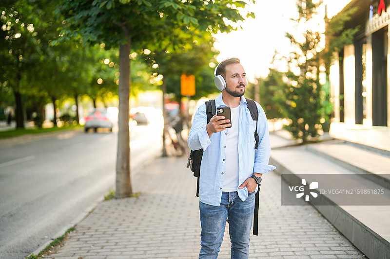 日落时分，在市中心一边听音乐一边看手机炒股的男人图片素材