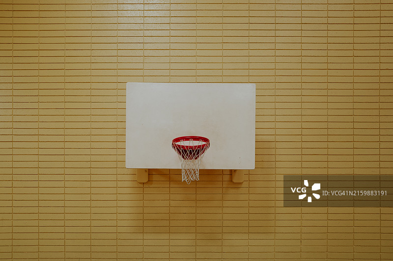 黄色砖墙上的白色篮球板和红色篮筐图片素材