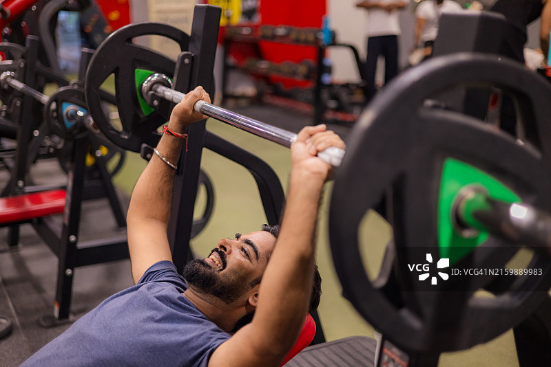 年轻男人在健身房用杠铃进行力量训练图片素材
