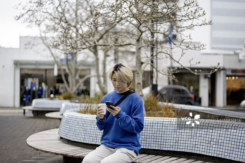 30多岁的亚洲女性坐在长椅上喝咖啡玩手机图片素材