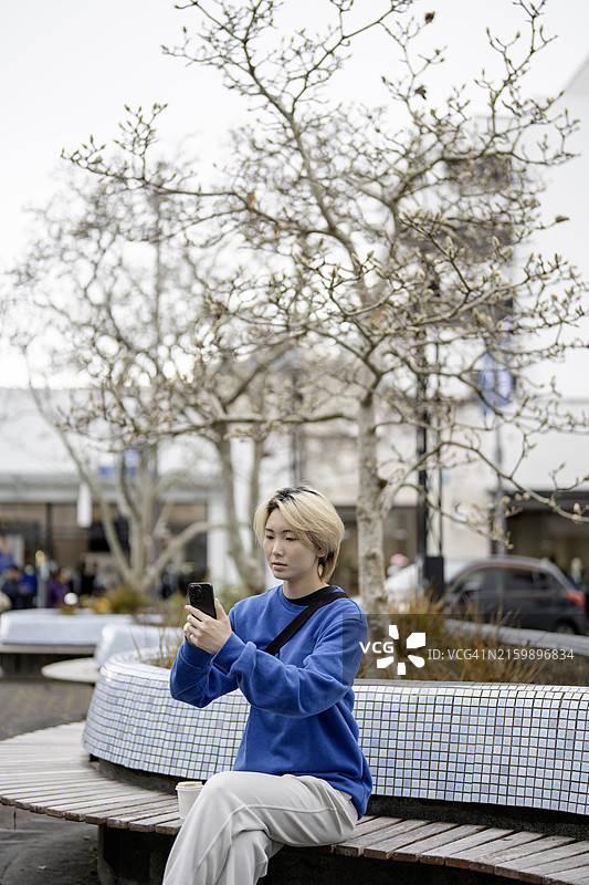 坐在户外长椅上拿着智能手机的亚洲年轻女性图片素材