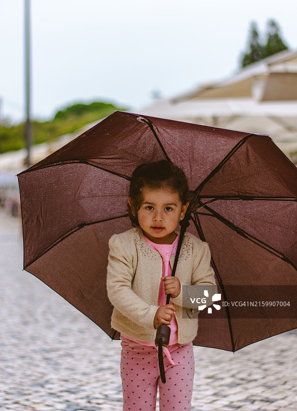 小女孩在里斯本雨中街道上行走图片素材