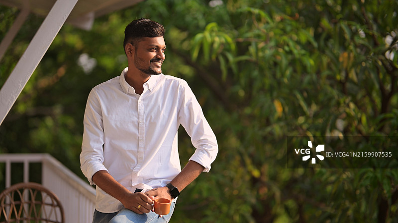 年轻男人在阳台上放松喝茶，欣赏宁静的户外景色图片素材