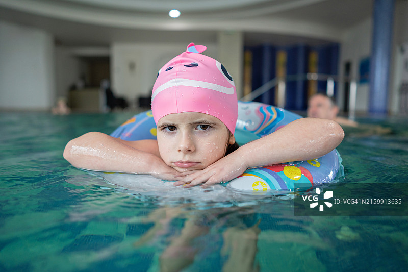 戴着泳帽的女孩在室内游泳池的充气泳圈上生气图片素材