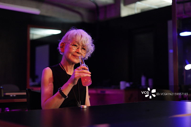在酒吧里喝鸡尾酒的亚洲年长妇女图片素材