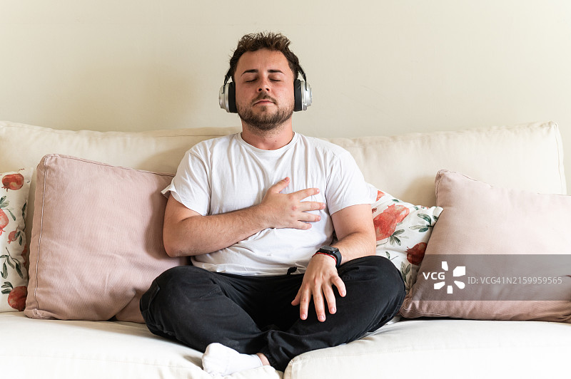 年轻男人在家里的沙发上戴着耳机听音乐放松图片素材