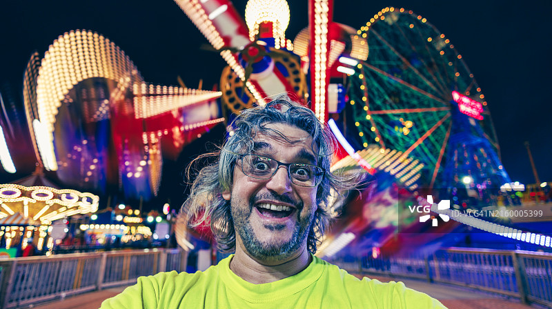快乐的中年男人在灯火通明的游乐园里自拍图片素材