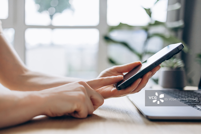 女士在笔记本电脑上工作时查看智能手机特写图片素材