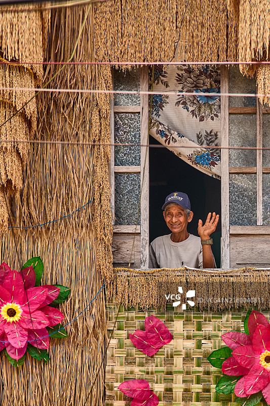 卢邦帕希亚斯节：一位老人从装饰着鲜艳农产品的房屋窗户中挥手致意图片素材