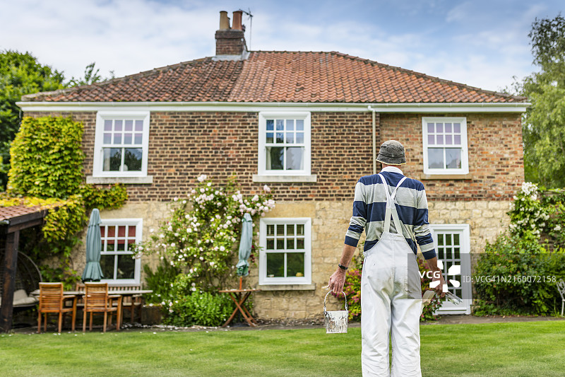 油漆工手持刷子和油漆罐观察房屋外观图片素材