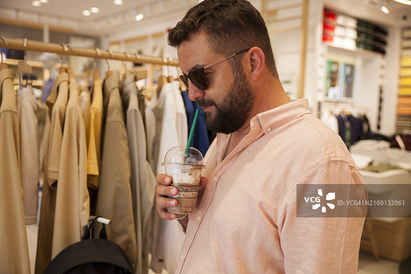 戴着黑色眼镜的男人在服装店喝咖啡并看衬衫图片素材
