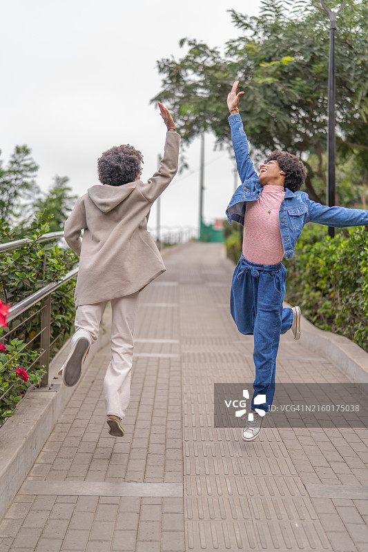 非裔美国双胞胎姐妹在公园里跳起来击掌图片素材