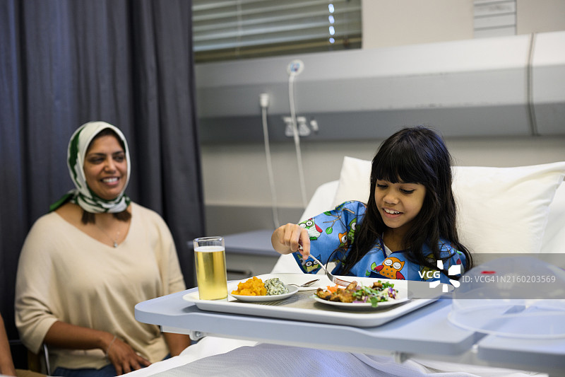 年轻的穆斯林女孩在医院里用餐，母亲坐在她旁边图片素材