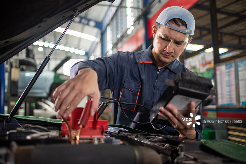 亚洲汽车维修技师用检测仪测试发动机，用万用表检测汽车电池电压图片素材