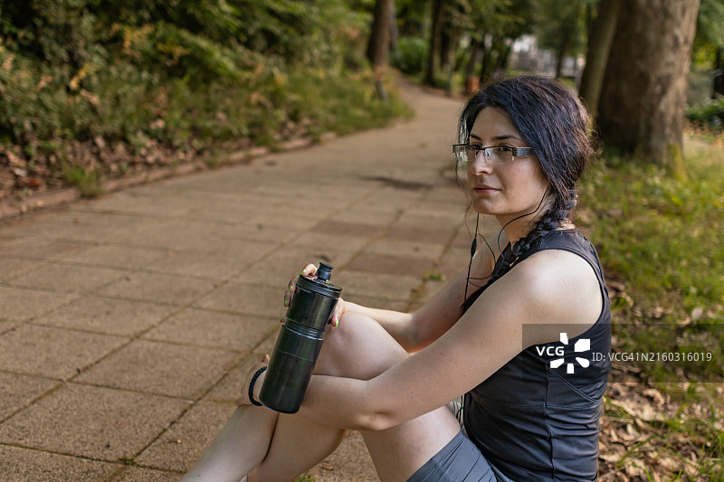 年轻健康女子在公园健身，训练后休息喝水图片素材