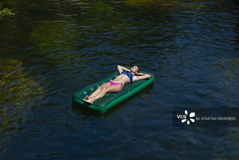 在山地湖泊中充气床垫上的比基尼女人图片素材