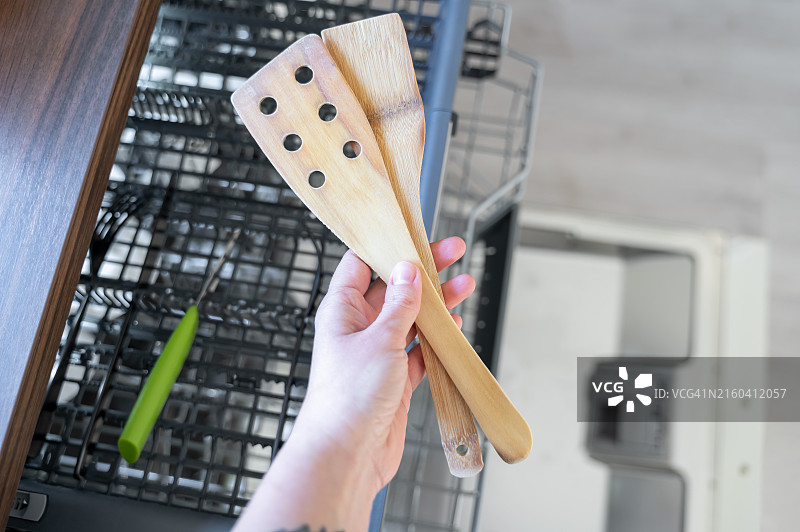 手持两个木制刮铲，靠近打开的洗碗机图片素材