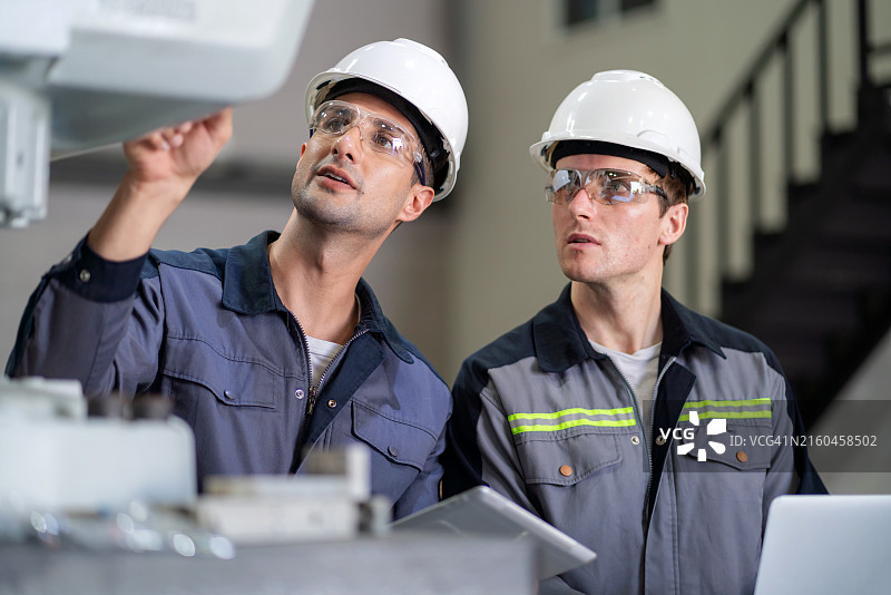 在先进的工厂里，专家工程师在装配线上精确管理大型机械臂，展示了先进的技术和工业创新。现代制造环境中的协作、效率和专业知识。图片素材