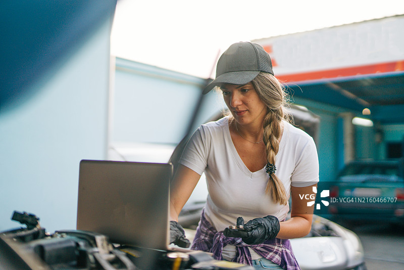 女汽车机械工使用笔记本电脑在汽车维修店调整ECU诊断分析监控引擎问题图片素材