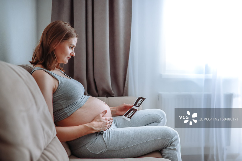 中年孕妇坐在沙发上，仔细观看超声波照片图片素材