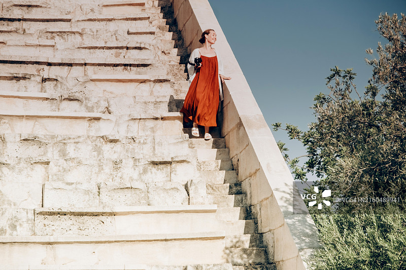 穿着飘逸长裙的女人走下古老圆形剧场的石阶，享受温暖的阳光图片素材