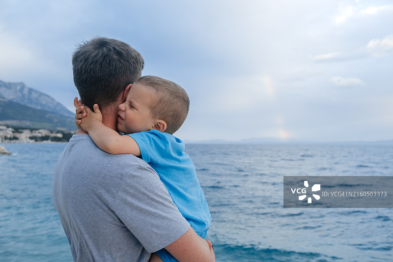 度假中的家庭：快乐的孩子拥抱他的父亲，父亲抱着孩子，以大海为背景图片素材