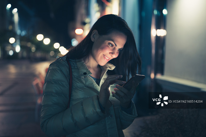 在城市夜间街道上使用智能手机的创新女性图片素材