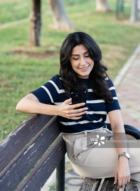 坐在公园长椅上使用手机的年轻女人图片素材