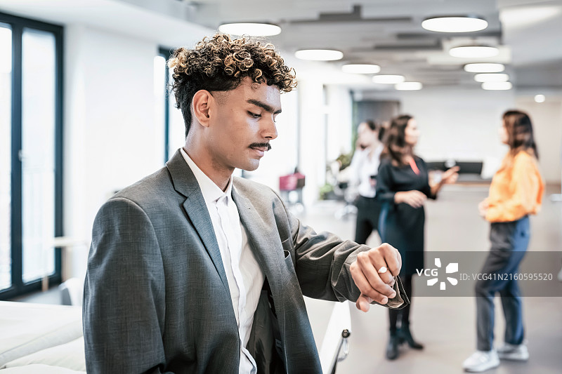 在办公室里看手表的年轻商人图片素材