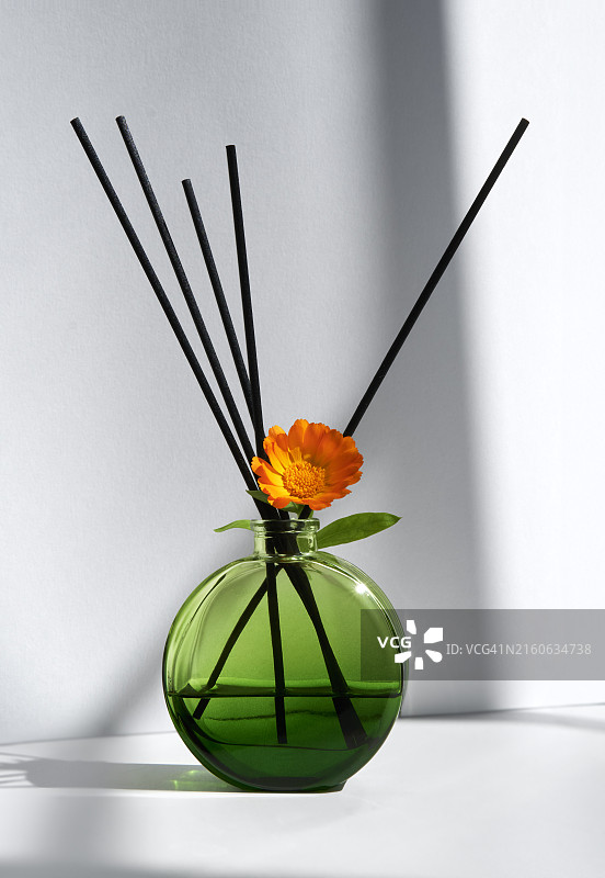 白色背景下带有金盏花和黑色香薰棒的绿色玻璃香薰图片素材