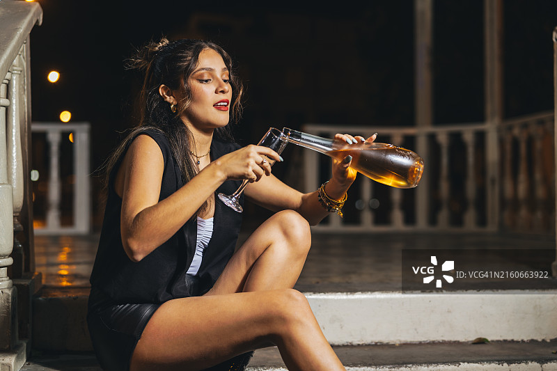 年轻女子坐在街上，给自己倒了一杯玫瑰酒图片素材