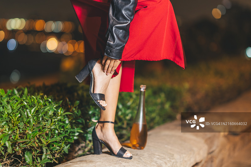 在街上扶着高跟鞋，站在一瓶葡萄酒旁的醉酒女人图片素材