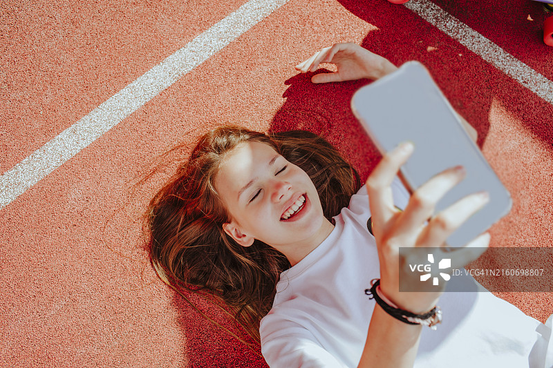 快乐的青少年女孩躺在地上用智能手机自拍图片素材
