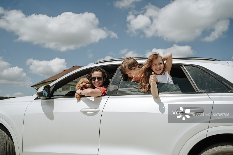 阳光明媚的日子里，快乐的一家人和Maltipoo狗狗在白色汽车里图片素材